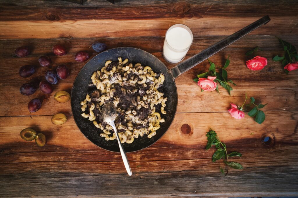 A rustic serving of pasta with milk, plums, and flowers on a wooden table.